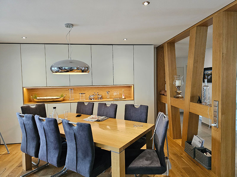 Innenaufnahme eines modernen Esszimmers in einem Holzhaus von Ettwein mit Holztisch, blauen Stühlen und Trennwand in Fachwerkstil – natürliches Wohnen dank nachhaltigem Holzbau.