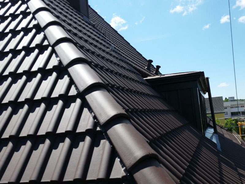 Nahaufnahme eines neuen dunklen Ziegeldachs mit Gaupe – langlebiger Dachbau mit hochwertiger Dachumdeckung aus Ziegeln.