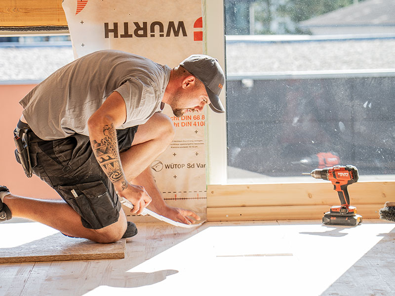 Ettwein Handwerker misst mit einem Zollstock den Boden in einem Holzhaus – präzise Arbeit und nachhaltiger Holzbau aus der Zimmerei und Schreinerei Ettwein.