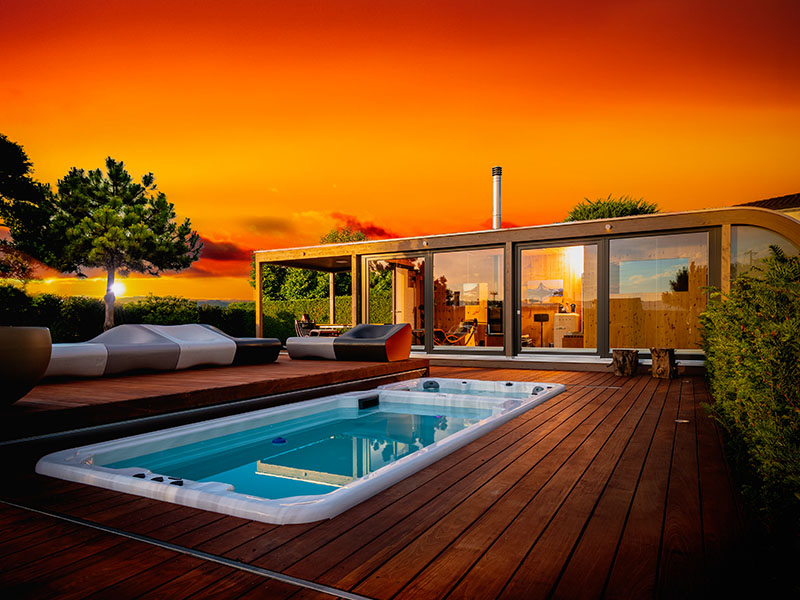 Luxus-Gartenhaus von Ettwein aus edlem Holzbau bei Sonnenuntergang mit Pool und Holzterrasse – handgefertigt in der Zimmerei und Schreinerei Ettwein.