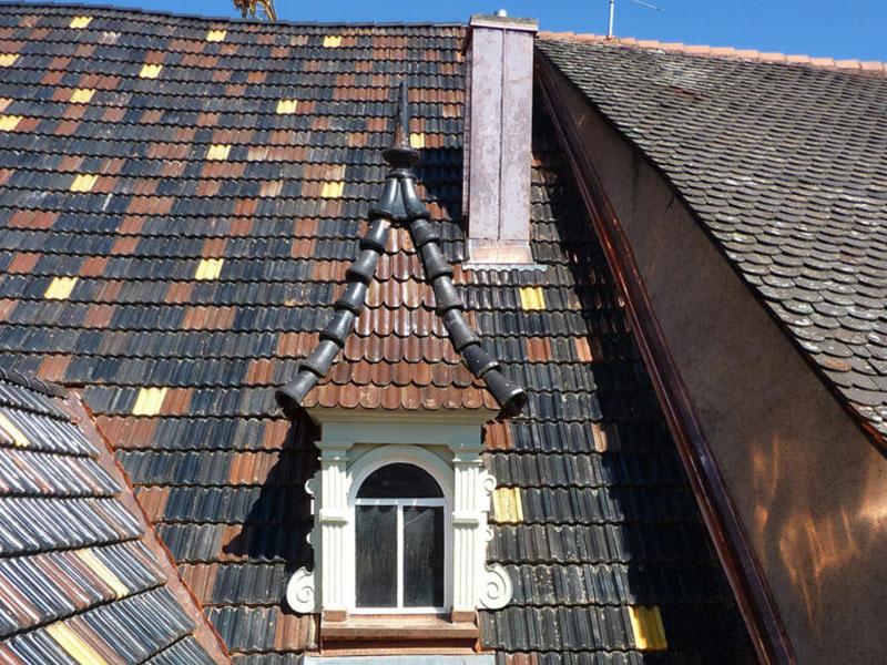 Nahaufnahme eines neuen Ziegeldachs mit Gaupe an einem historischen Gebäude – gemischte Ziegel in Braun, Gelb und Dunkel für eine authentische Dachsanierung.