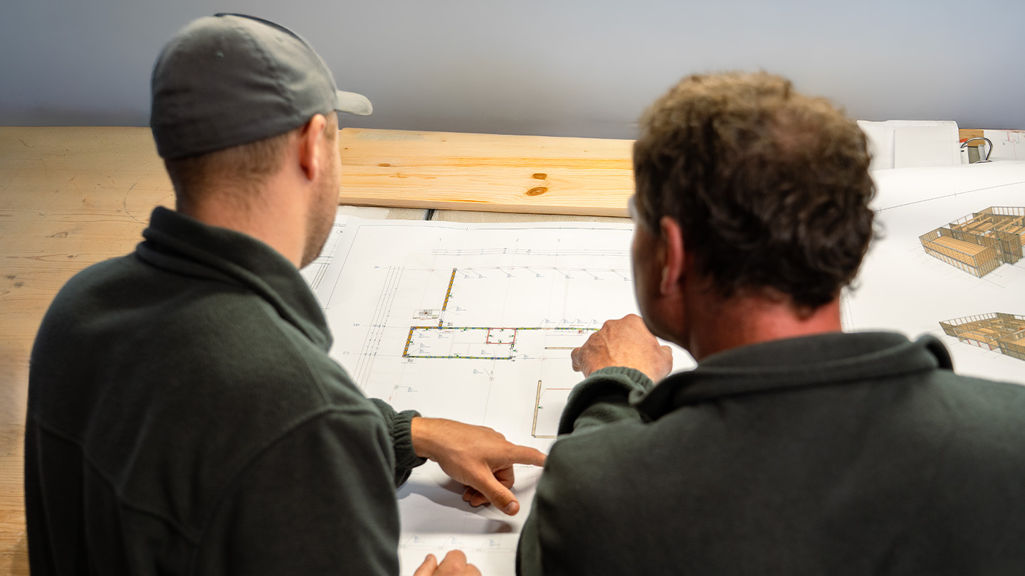 Zwei Mitarbeiter im Holzbau von Ettwein betrachten gemeinsam einen Bauplan auf einem Holztisch – Planung und Konzeptentwicklung für kommunale Neubauten, Kitas und Schulen.
