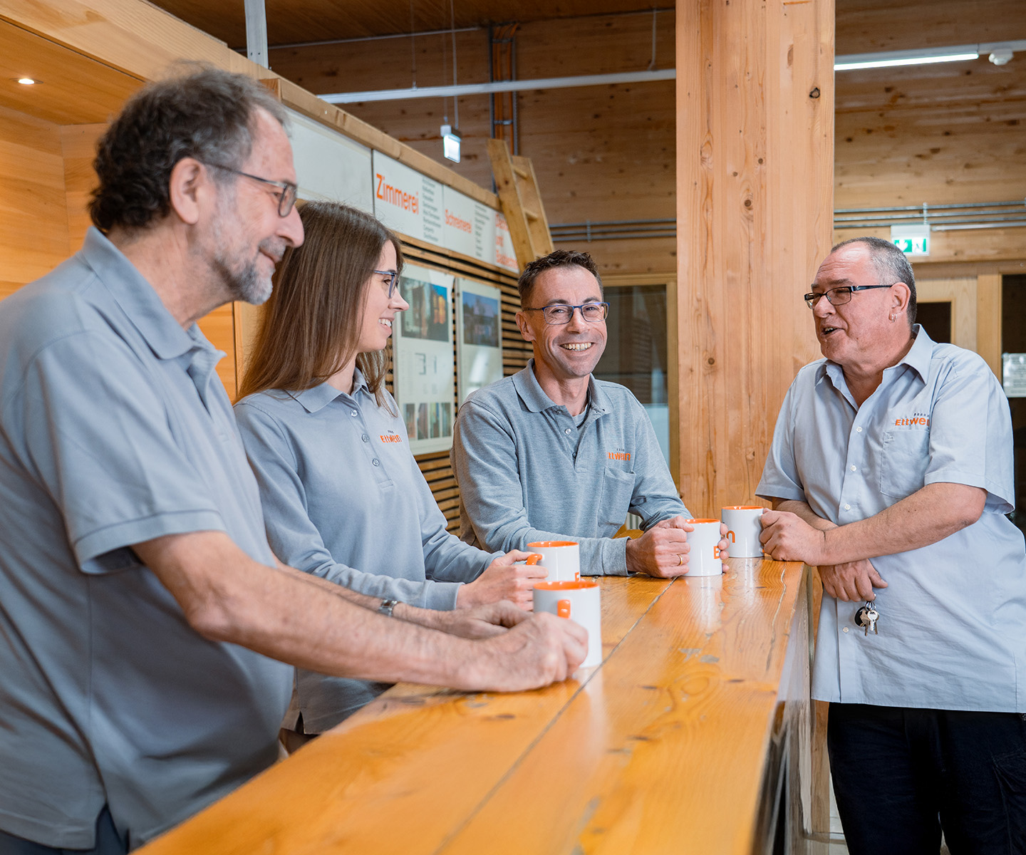 Vier Ettwein‑Mitarbeiter im lockeren Gespräch in den Betriebsräumen — Ettwein, Job Holzbau, Ausbildung Zimmerer, Stellenanzeige Schreiner.