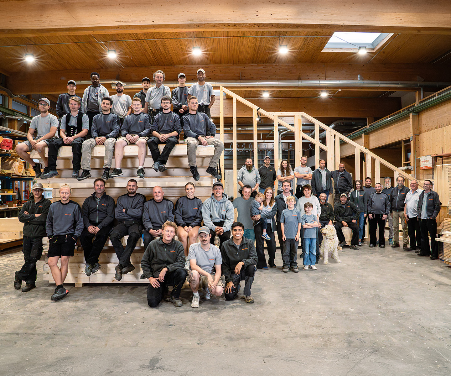 Komplettes Ettwein Team in der Fertigungshalle vor Maschinen und Holzelementen — Ettwein Zimmerei, Familienbetrieb, Holzbau, Handwerksbetrieb.