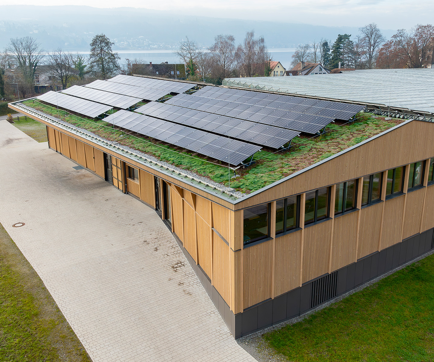 Luftaufnahme des Produktionsgebäudes des Winzervereins Insel Reichenau am Bodensee – moderner Holzbau mit Photovoltaikanlage auf begrüntem Dach.