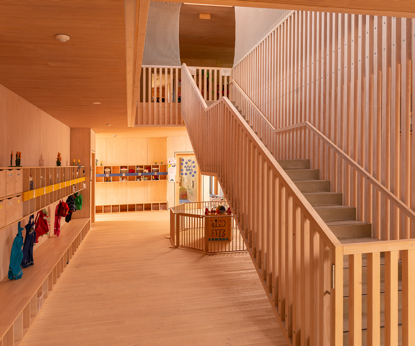 Innenraum einer modernen Kita in Holzbauweise mit Holzboden, Holzdecke, Holztreppe und Garderobe – nachhaltiger Holzbau für Kommunen, Kitas und Schulen im Neubau.