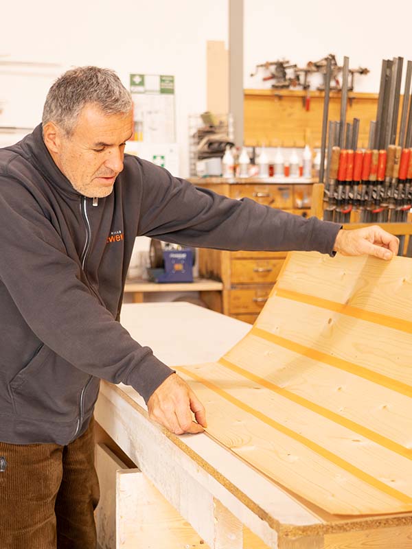 Ettwein-Mitarbeiter prüft ein dünnes Holzbauteil für die Möbelreparatur und kontrolliert die verbundenen Platten.