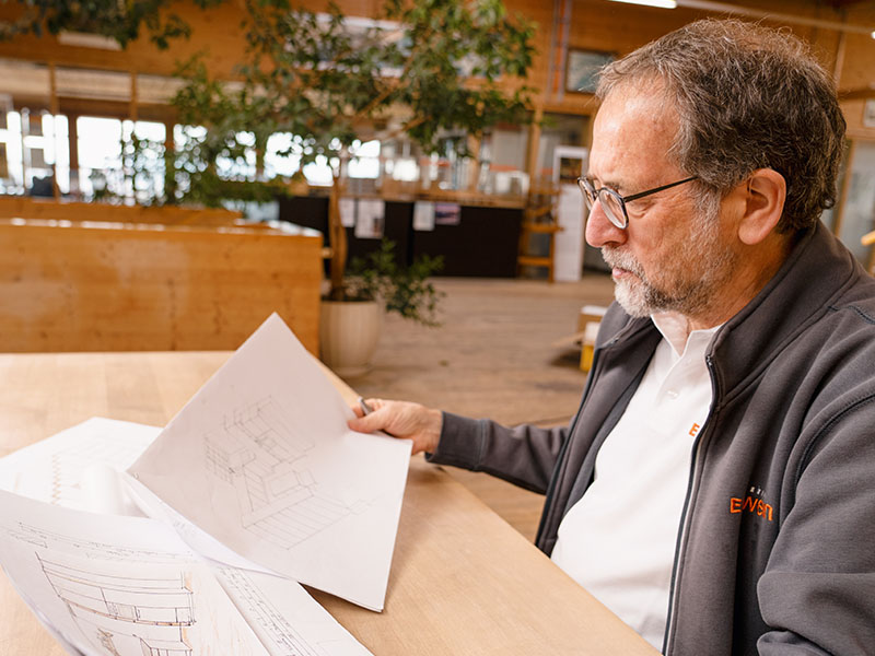 Älterer Ettwein-Mitarbeiter betrachtet eine Projekt-Skizze am Holztisch – sorgfältige Planung für hochwertigen Innenausbau.