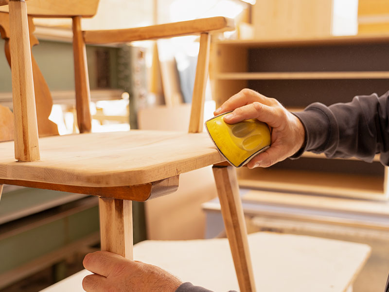 Detailaufnahme eines Ettwein-Mitarbeiters, der einen alten Holzstuhl abschleift – präzise Möbelreparatur und Oberflächenbehandlung.