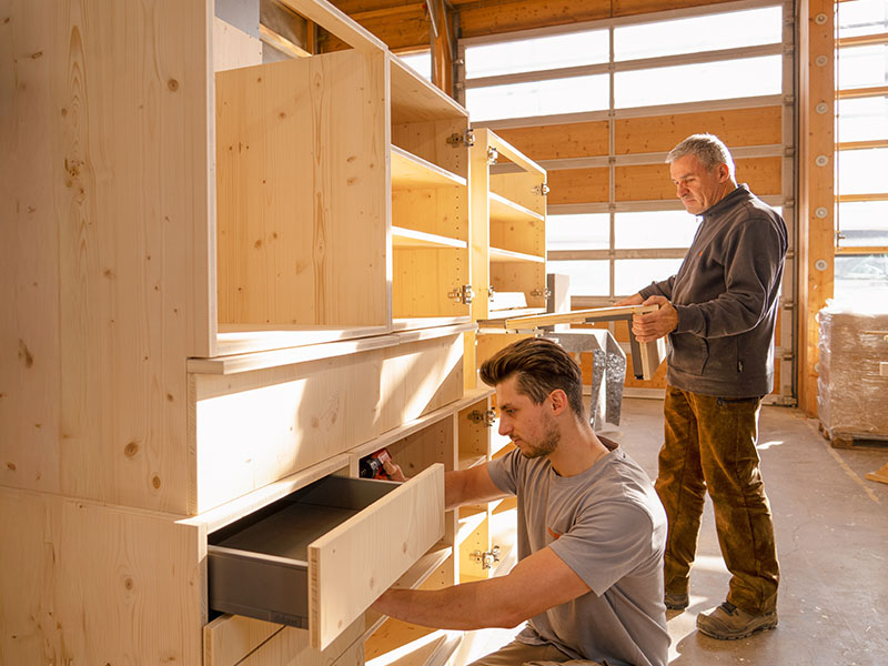 Zwei Ettwein-Mitarbeiter bauen gemeinsam einen maßgefertigten Holzschrank – präzises Handwerk in der Schreinerei für individuelle Möbel.